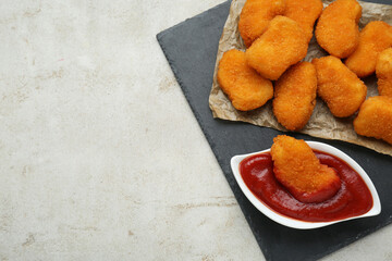 Tasty chicken nuggets with ketchup on light grey textured table, top view. Space for text