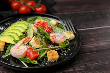 Delicious salad with croutons, avocado and shrimp served on wooden table, closeup. Space for text