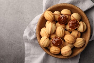 Delicious nut shaped cookies with boiled condensed milk in wooden bowl on gray textured table, top view