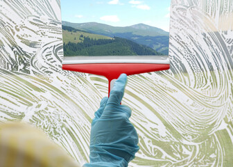 Worker cleaning window with squeegee, closeup. View through clear glass on picturesque mountains