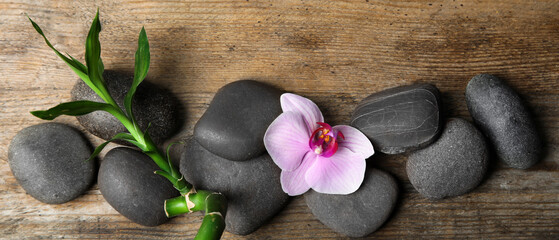 Fototapeta na wymiar Spa treatment. Flat lay composition with stones, bamboo and orchid flower on wooden table. Banner design