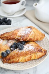 Fresh tasty puff pastry with sugar powder and blueberries served on white marble table, closeup