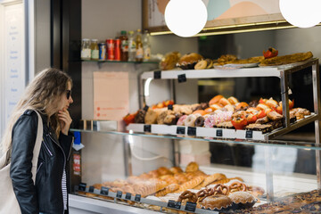 Woman looks at showcase with colorful cakes 