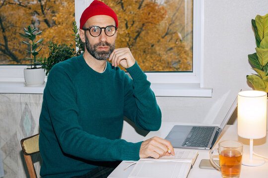 Adult man in a red winter hat at the workplace in his home office.