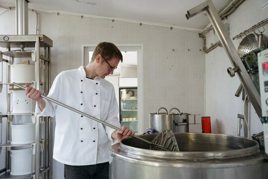 A worker at a cheese factory cuts cheese in a pasteurizer