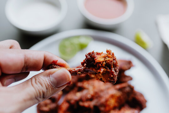 Hand Of Man Eating And Holding Spicy Chicken Wings With Buffalo Sauce. Food On A Rustic Background With Copy Space. Top View