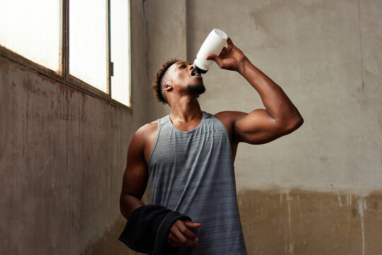 Confident athletic guy drinking water in shabby gym