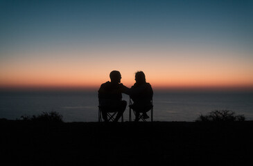 Happy sitting couple enjoying sunset ocean view
