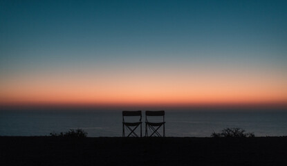 Empty camping chairs on ocean lookout at sunrise