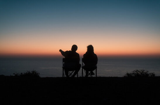 Sitting couple silhouette looking at the sea during sunset