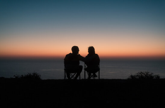 Happy sitting couple enjoying sunset ocean view