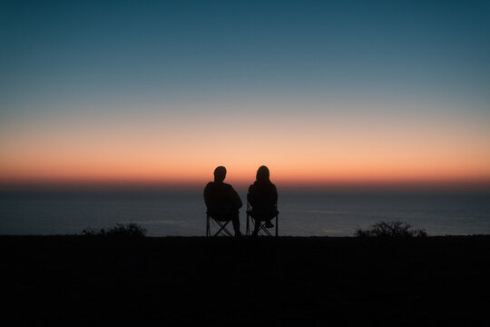 Sitting couple silhouettes enjoying sunset sea view