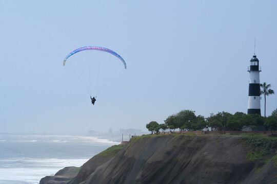 Paragliding is action sport in Lima Peru. Person is paragliding in Miraflores Lima Peru with lighthouse and buildings background.. Selective focus. Open space area.