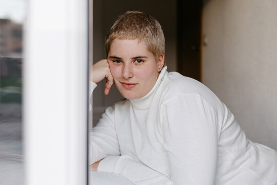 Calm young androgynous leaning on hand in bedroom