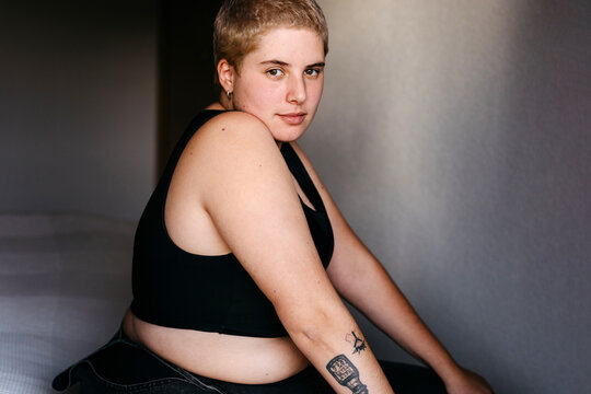 Sensual tattooed non binary model sitting on bed