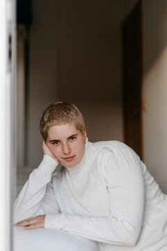 Calm non binary person sitting near bed in apartment