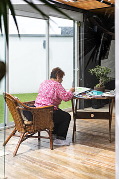 Wide shot of senior lady having good time drawing at home