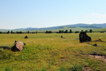 Ancient burial stones in the endless steppe at the foot of a high mountain range.