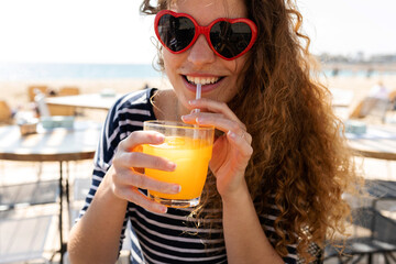 Obraz premium Trendy joyful woman drinking juice at beach restaurant
