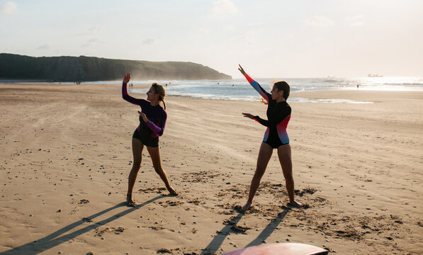 Female surfers warming up on beach at sunset