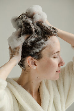 Young woman with hands touching her wet, soapy hair with shampoo foam