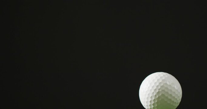 Close up of golf tee and ball on grass and black background, copy space, slow motion