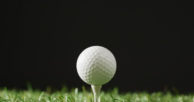 Close up of golf tee and ball on grass and black background, copy space, slow motion