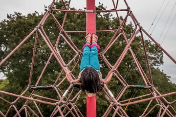 Girl lying down on climbing rope structure at a park