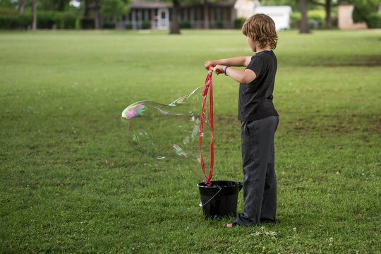 Boy standing in neighborhood field playing with giant bubble maker