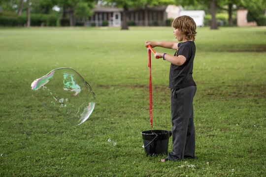 Boy standing in neighborhood field playing with giant bubble maker