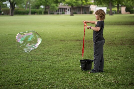 Boy standing in neighborhood field playing with giant bubble maker