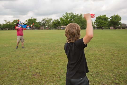 Father and son flying kite in neighborhood field into dramatic clouds