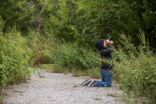 Young boy photographing trees on a gravel trail