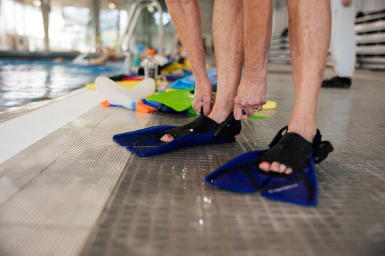 Woman in bathing suit putting on flippers at pool.