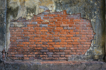 The plaster of an old weathered wall is flaking off in the middle. Below you can see a red brick...