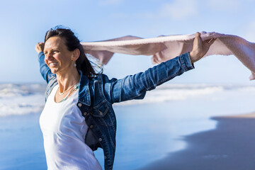 Woman walking at the beach while holding a scarf on the wind