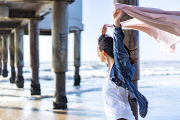 Woman walking at the beach while holding a scarf on the wind