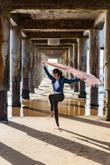 Woman dancing under a pier holding a scarf on the wind.