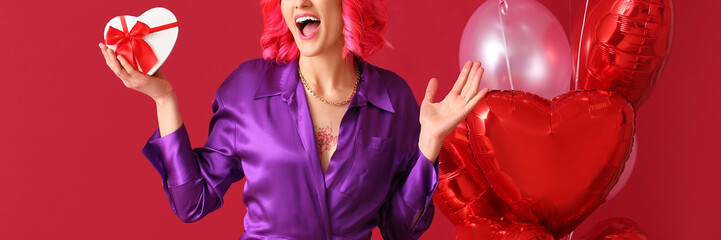 Surprised woman with heart-shaped gift and balloons on red background. Valentine's Day celebration