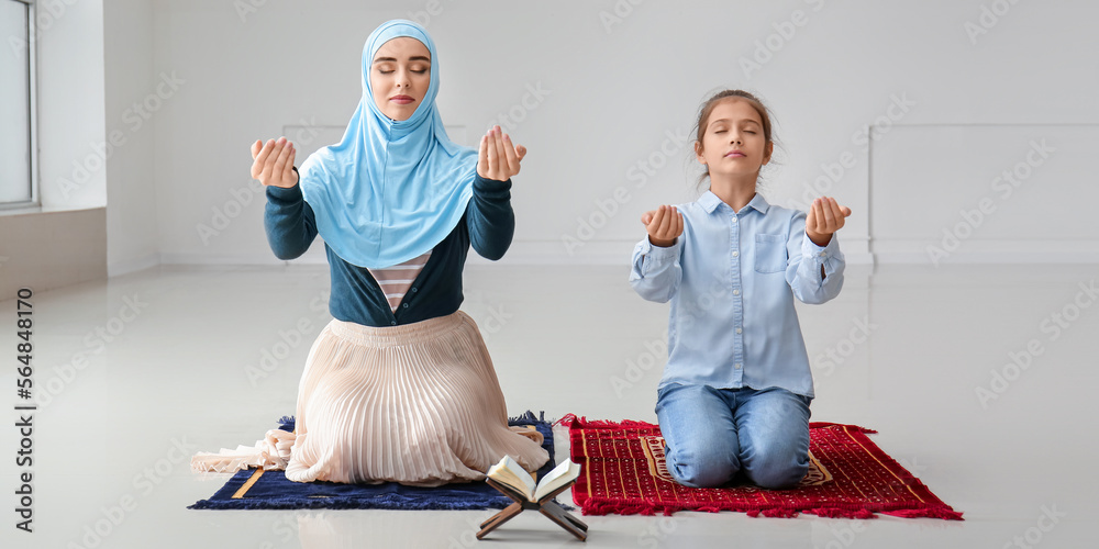 Wall mural Young Muslim woman with daughter praying indoors