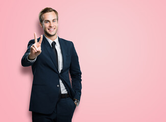 Excited businessman in confident black suit showing two fingers or victory sign gesture, on rose...