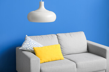 Grey sofa with cushions and hanging lamp near blue wall