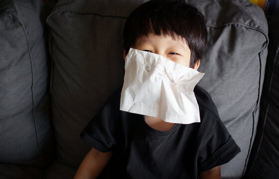 Cute little asian boy is wiping his nose while laughing