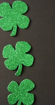 Vertical video of of st patrick's green shamrock leaves with copy space on black background