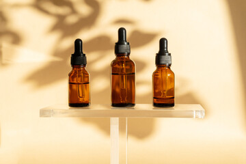 Three glass vials of amber-colored serum with dropper lid on transparent shelf. Essential oil for...