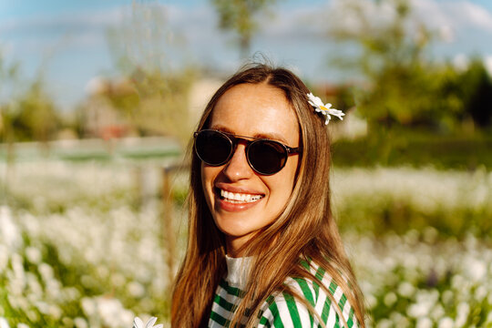 Woman in sunglasses smiles broadly with chamomile flower in her hair