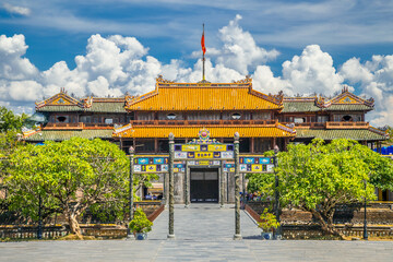 An ancient temple with an ornate gateway and roofing details under puffy white clouds at Hue in Vietnam