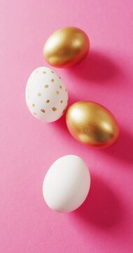 Vertical video of white and gold easter eggs on pink background