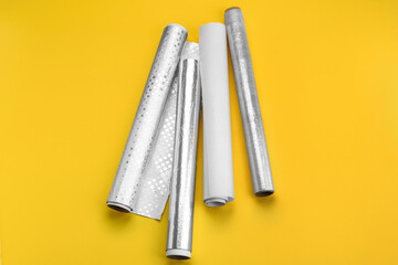 Rolls of aluminium foil, baking paper and food film on yellow background
