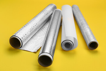 Rolls of aluminium foil, baking paper and food film on yellow background, closeup